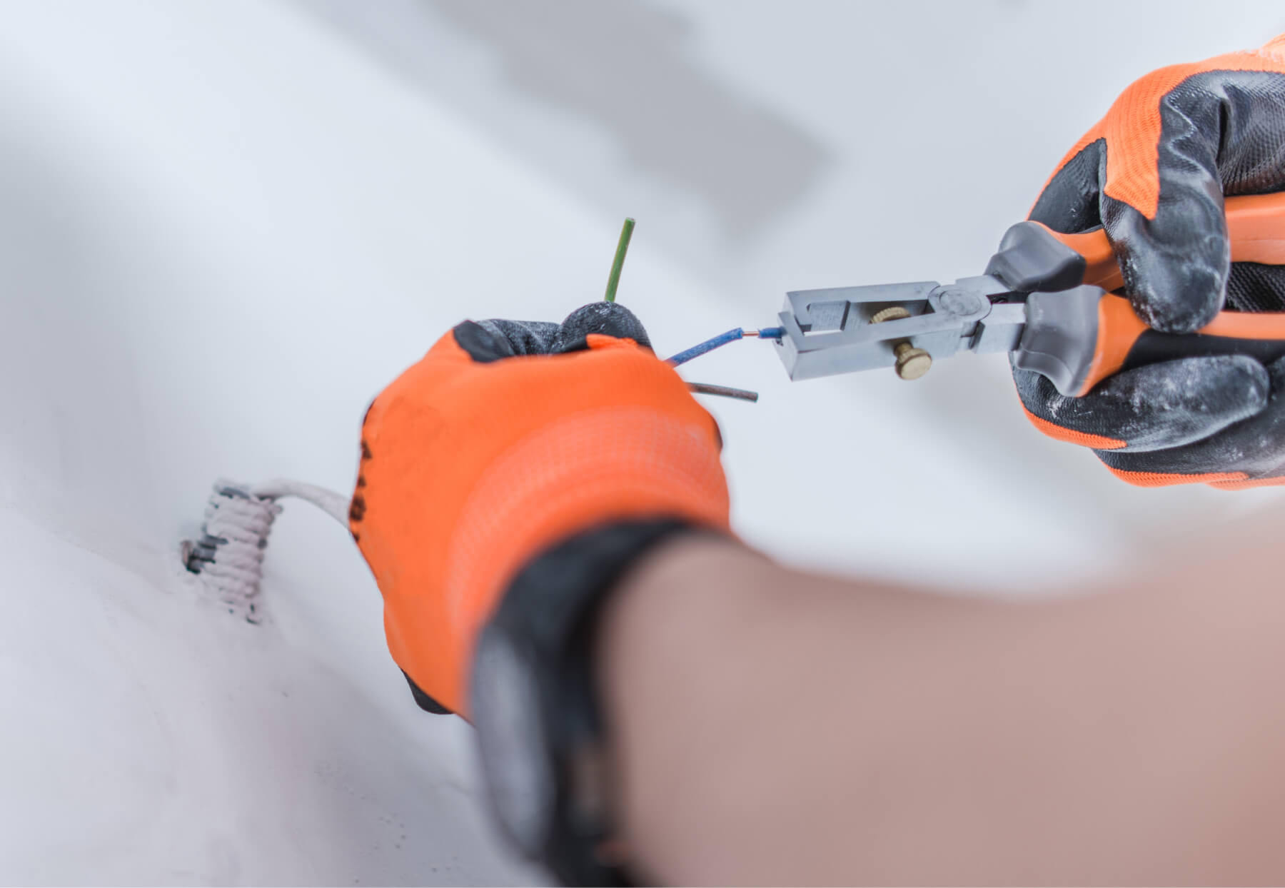 Gloved hands stripping the end of a wire coming out of a wall