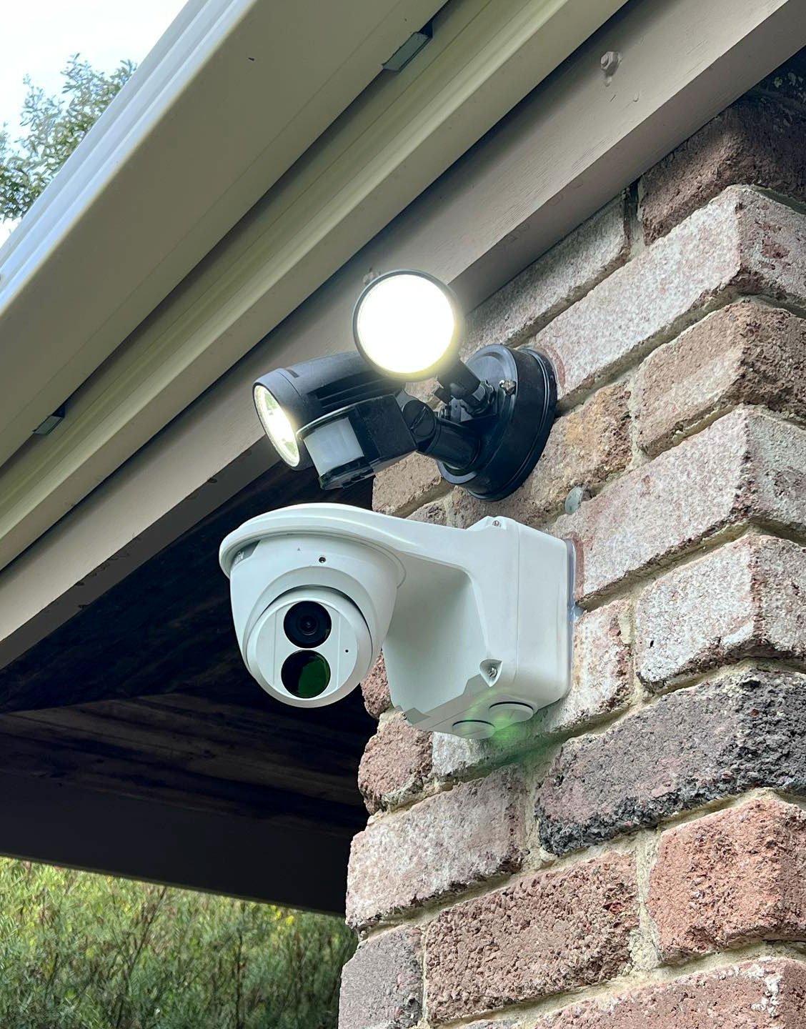 Security camera and twin floodlight mounted under a brick house eave