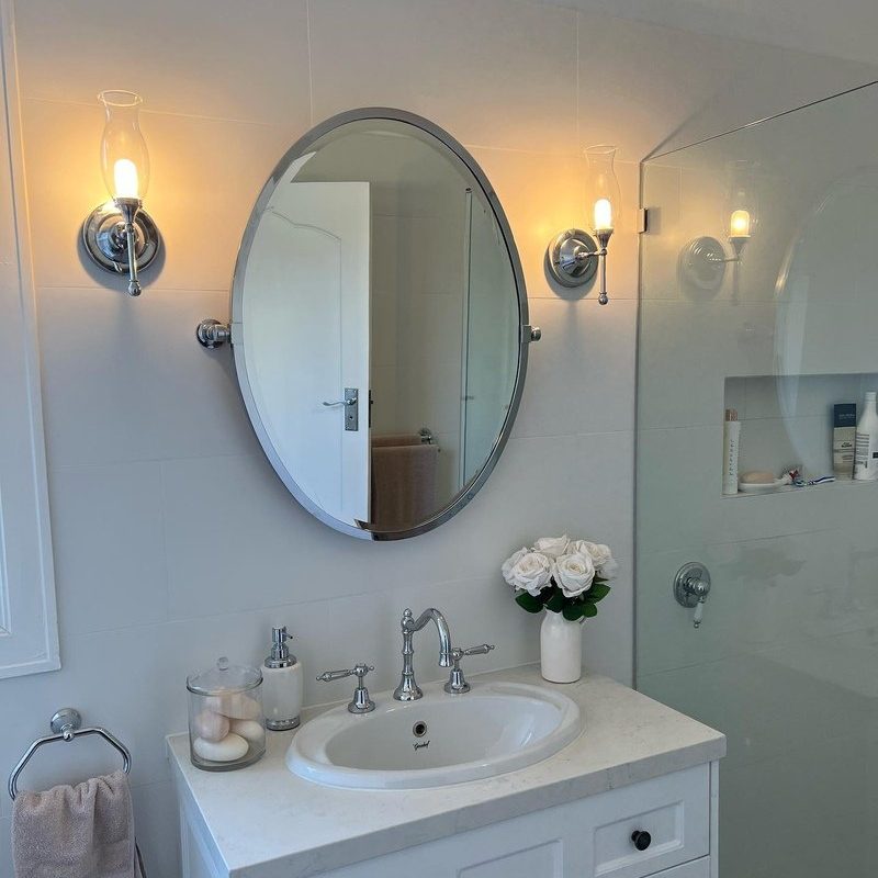Bathroom vanity with an oval mirror between two glass wall lights