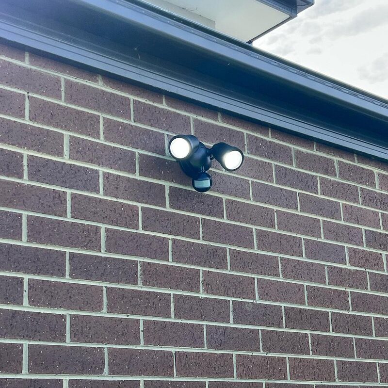Twin sensor floodlight mounted on a brick wall below the eave