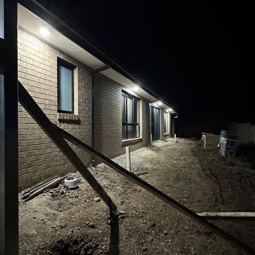 Side of a new brick house lit at night by downlights in the eaves