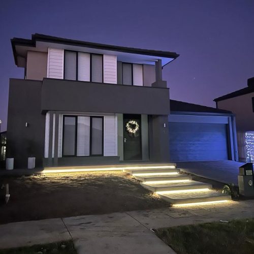Two-storey house at dusk with lit front steps and a lit garage door